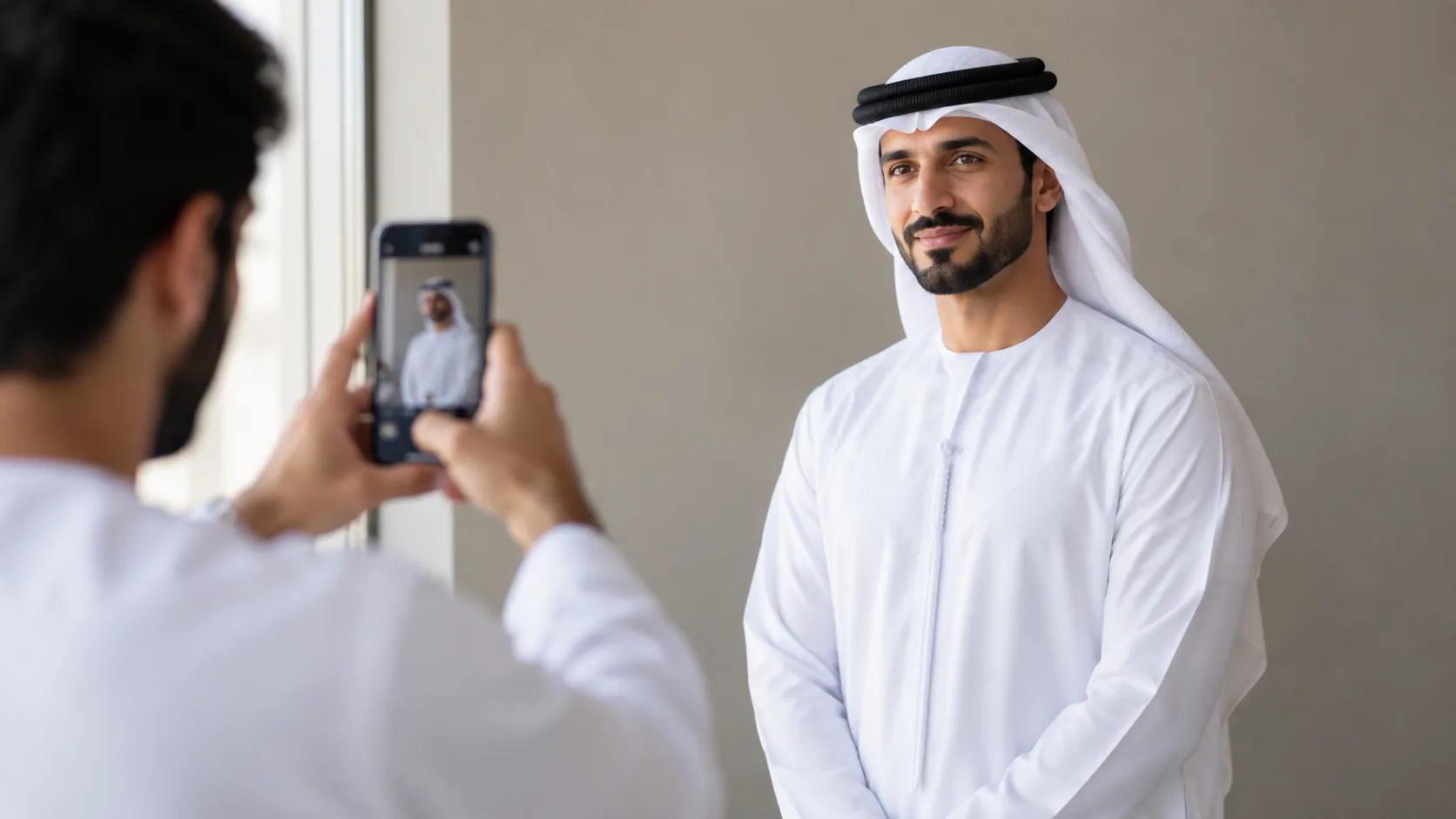 A professional man in a dishdasha having a headshot taken against a plain wall in natural light