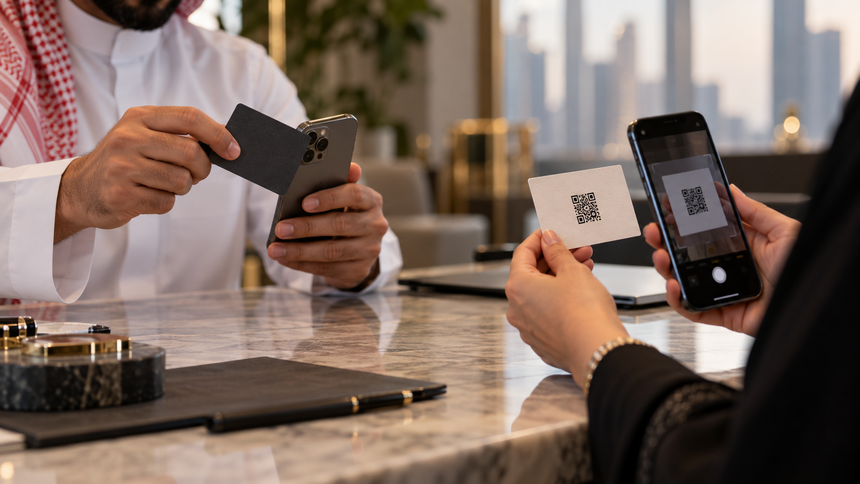 One person tapping a business card against a phone while another scans a QR code on a card, at a meeting table